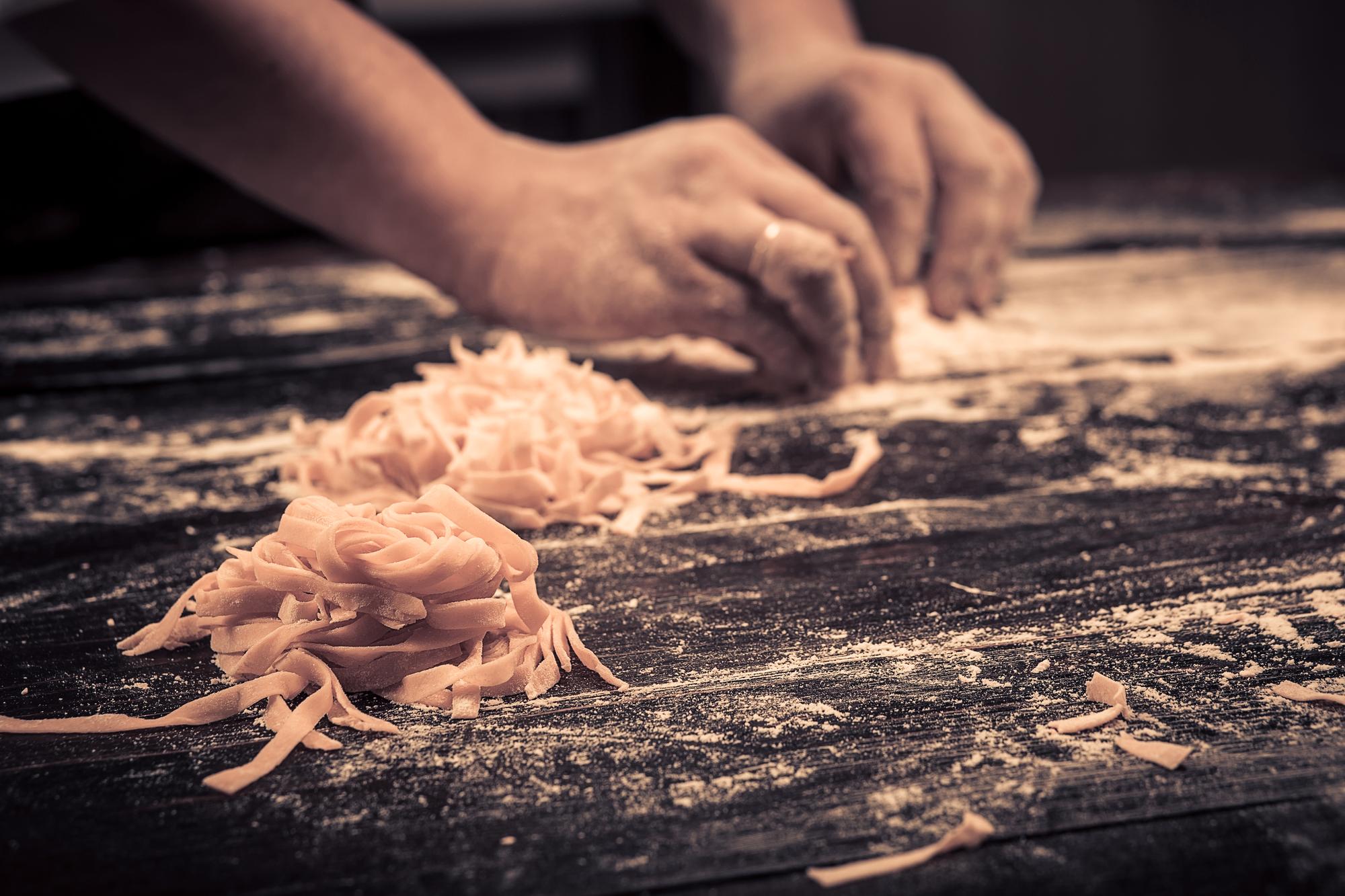Hands preparing fresh pasta on a wooden board